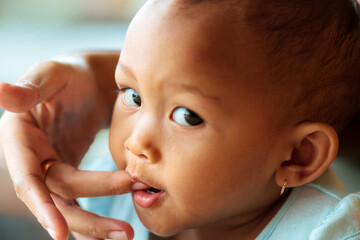 Southeast Asian baby girl biting mom's fingertip as her growing milk teeth causes itchiness on her gums