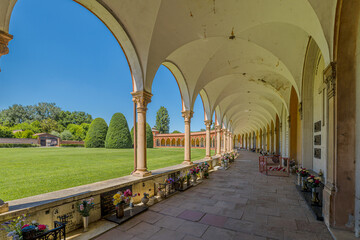 Ferrara, Italy - May 17, 2025: Ancient cemetery cloister featuring hanging lamps, tombs, and sculptures in the 15th-century Charterhouse of Ferrara, set against a lush green lawn