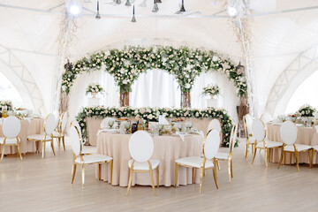 Elegant wedding reception hall featuring round tables, white and gold chairs, and floral arrangements