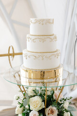 Elegant white wedding cake decorated with gold standing on glass and gold stand with flowers