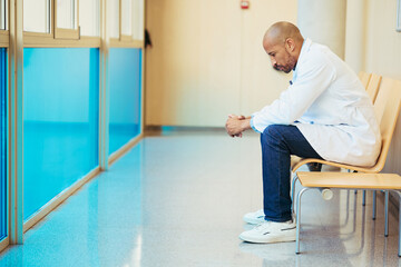 Concerned doctor sitting in hospital corridor reflecting on patient health