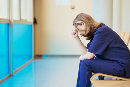 Exhausted nurse sitting in hospital corridor reflecting on difficult day