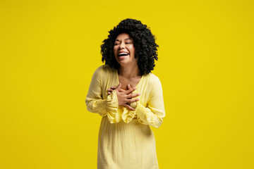 Young woman laughing with hands on her chest on yellow background