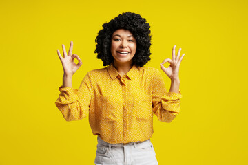 Young woman showing ok sign with both hands and smiling on yellow background
