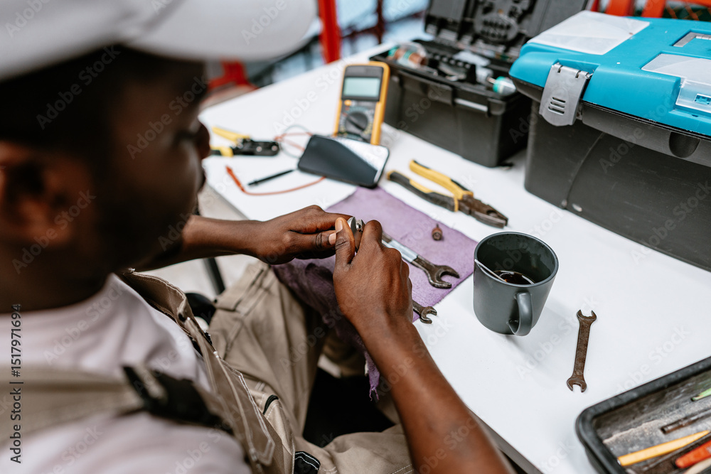 Poster technician repairs tools in workshop while sitting at desk with various instruments and materials