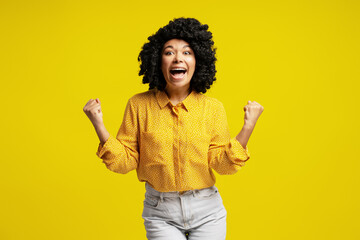 Enthusiastic woman celebrating with raised fists on yellow background