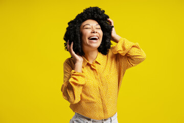 Carefree young woman with afro hair laughing out loud touching her hair on yellow background