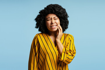 Young woman suffering from strong toothache touching cheek with hand