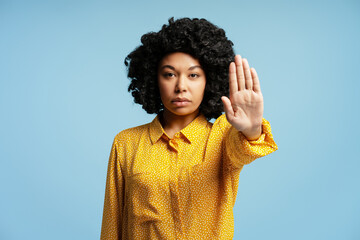 Serious young woman showing stop gesture with hand on blue background