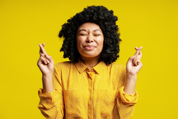 Young woman crossing fingers making a wish on yellow background