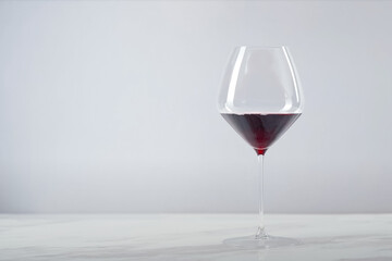 Single glass of red wine placed on a white marble surface with a light gray background, creating a minimal and elegant composition

