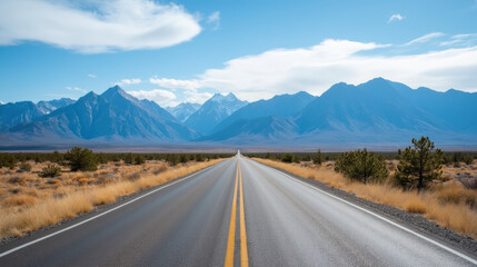 Scenic road stretches through vast landscape, flanked by majestic mountains and golden grasslands under bright blue sky