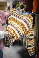 Young woman choosing clothing at a thrift store, sustainable and reused fashion.