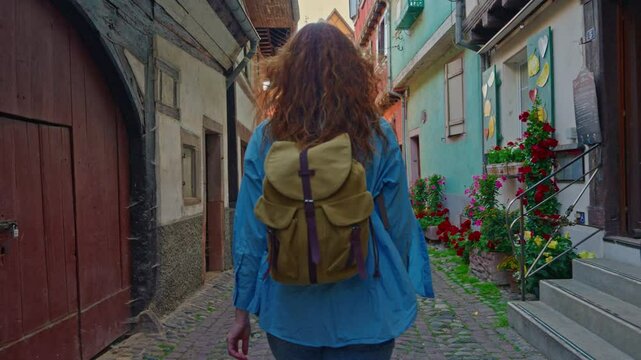 Woman with backpack walking on the beautiful street full of colorful houses with flowers of Eguisheim, France 
