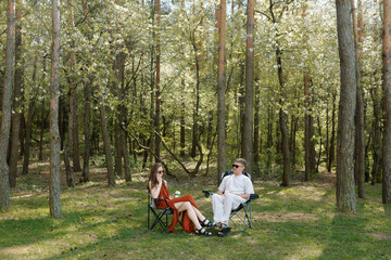 Couple relaxing in folding chairs under trees in sunny peaceful forest setting