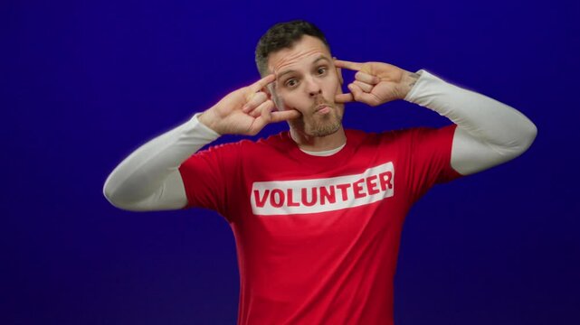 Man in volunteer shirt playfully posing against vibrant blue background showing humor fun volunteerism.