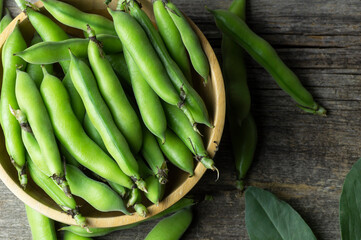 Fresh broad beans with pod in bowl on wooden background, healthy food