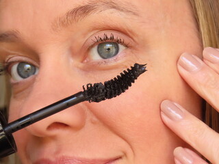 Closeup of woman applying black mascara on her eyelashes with a curved brush. Woman applying eyelash makeup. Woman in her forties doing her beauty routine.