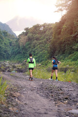 Obraz premium Hikers Walking on Rocky Trail Toward Mountain Surrounded by Lush Green Forest