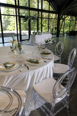 Formal dining table with elegantly arranged glassware, plates, and green napkins. Central floral arrangement features white roses and candles, creating a refined atmosphere.