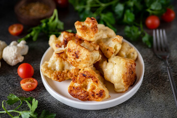 Hearty lunch: cauliflower in batter on a white plate on a gray background. Close-up