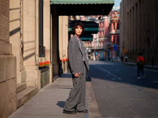 Portrait of handsome Chinese young man wearing gray suit posing in the street, young guy with black curly hair with urban background. Male fashion, cool Asian young man lifestyle.