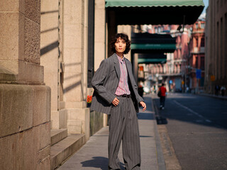 Portrait of handsome Chinese young man wearing gray suit posing in the street, young guy with black curly hair with urban background. Male fashion, cool Asian young man lifestyle.