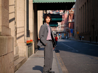 Portrait of handsome Chinese young man wearing gray suit posing in the street, young guy with black curly hair with urban background. Male fashion, cool Asian young man lifestyle.