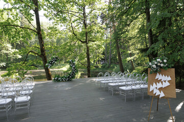 Elegant outdoor wedding ceremony setup in a lush forest setting featuring a floral arch by the...