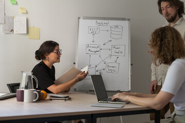 Three software developers brainstorming in a modern office. Team coding session with laptops...