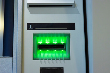 A closeup of a glowing green card slot of an ATM, ready to accept a transaction card.