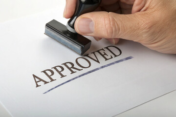 Hand stamping the word approved on a white sheet of paper signifying acceptance or agreement