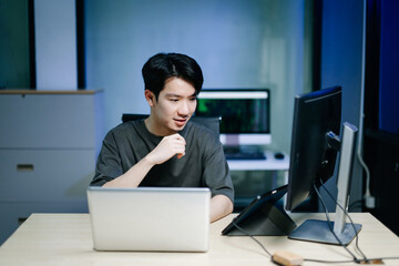 Young male programmer working with tablet and screen displaying code. Modern tech office setup, great for software, coding, IT