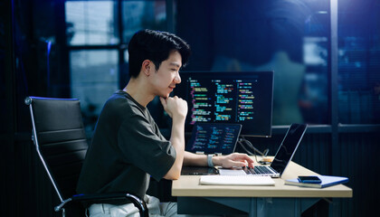 Asian developer writing code at night in modern office setup. Concept of software engineering, programming, digital workspace