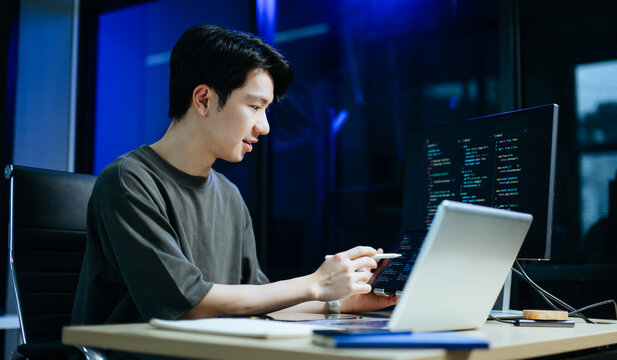 Young male programmer working with tablet and screen displaying code. Modern tech office setup, great for software, coding, IT..