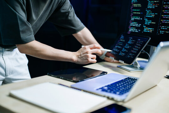 Programmer using stylus and laptop to write code at night. Coding workspace with tablet, monitor, and dark theme