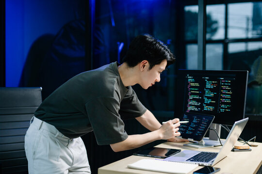 Young male programmer working with tablet and screen displaying code. Modern tech office setup, great for software, coding, IT..