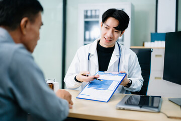 Asian doctor points to a medical form while consulting a patient in a bright clinic office. Concept...