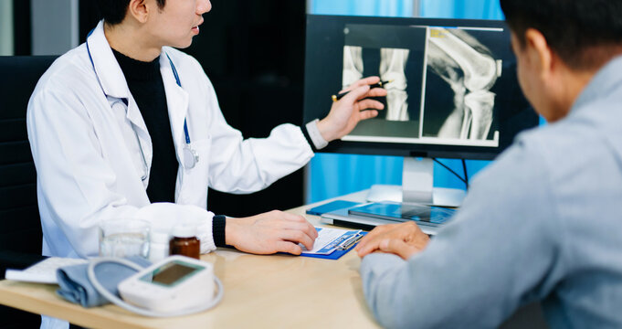 Asian doctor discusses knee X-ray results with senior patient in modern clinic. Concept of orthopedic consultation, bone care, health diagnosis