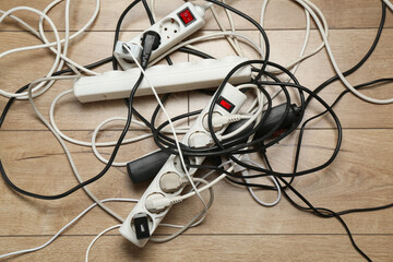Extension power boards overloaded with plugs on wooden floor, top view