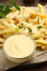Delicious cheese sauce in bowl, French fries and parsley on table, closeup