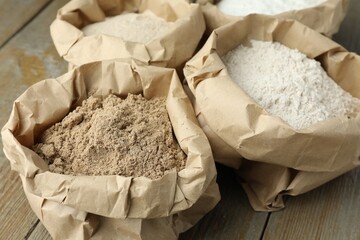 Different types of flour in paper bags on wooden table, closeup
