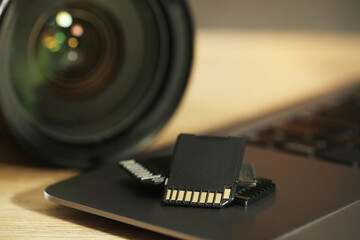 SD memory cards, laptop and photo camera on wooden table, closeup