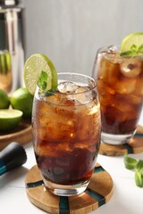 Tasty Cuba Libre cocktail in glasses, ingredients and muddler on white table, closeup