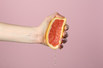 Woman squeezing grapefruit on pink background, closeup