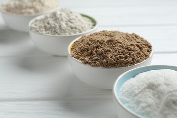Different types of flour in bowls on white wooden table, closeup
