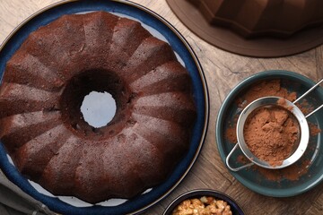 Tasty chocolate bundt cake, walnuts and cocoa powder on wooden table, flat lay