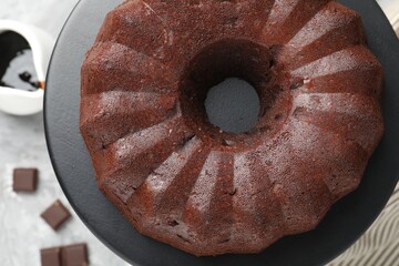 Tasty bundt cake, pieces of chocolate and sauce on table, flat lay
