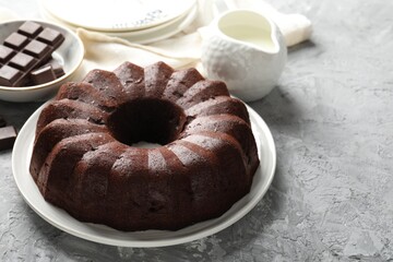 Tasty bundt cake, pieces of chocolate and milk on grey table, closeup. Space for text