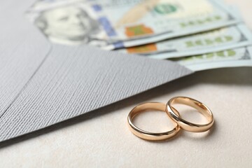 Two gold wedding rings, dollar banknotes and envelope on white table, closeup